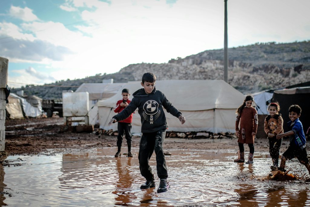 pexels-photo-10629419-10629419 Children splash in a muddy puddle at a refugee camp in Idlib, Syria, capturing resilient spirit.